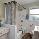 The crisp, newly-updated full bathroom serves the floor, featuring a new shower surround, toilet, vanity, LED lighting, luxury vinyl plank flooring, original medicine cabinet, wainscoting, and built-in makeup desk and drawer. 