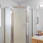 The modern hallway bathroom is shared by the front and middle bedrooms, featuring a bright window, an obscured glass-encased shower, a tile countertop, and updated vanity lighting.