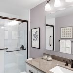 Refreshed ¾ bath with sleek vanity, quartz-style counters, and an easy-step shower with clear glass doors and dual grab bars.