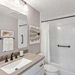 Freshly updated full bath with sleek quartz-look counters, bronze fixtures, and accessibility grab bars for ease and safety.