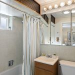 Full bath with tub/shower, mirrored storage, and natural light—simple and functional, with vintage charm.