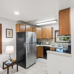 The kitchen offers classic wood cabinetry, granite-look Formica counters, and a full suite of appliances. Durable tile underfoot and a window above the sink keep it light and functional.