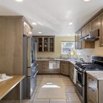 U-shaped for efficiency and framed by soft archways, the kitchen features Formica counters, stainless appliances, tile flooring, and custom cabinetry.