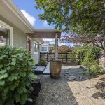 Inside the fence, gravel, stone, sculptural plantings and mature canopy give the front grounds a distinctly Japanese-garden feel.