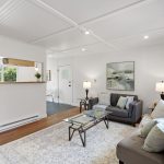 The red door opens straight into the living room—old-growth fir underfoot, paneled-and-beamed ceiling overhead, and a clear sightline toward kitchen and dining.