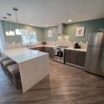 The clubhouse kitchen is spacious and like-new, with quartz counters, stainless appliances, and an open pass-through to the adjoining dining and living area.