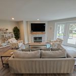 The clubhouse living area centers on a fireplace, with comfortable seating and direct access to the outdoor gathering space.